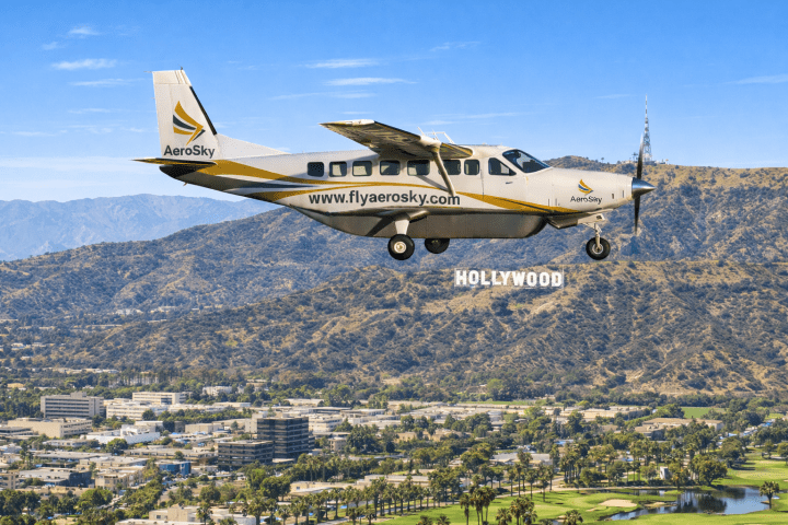 Small airplane flying over Hollywood sign with mountain background on a clear day.