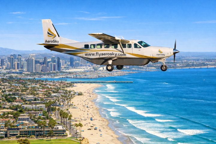 Small airplane flying over a city coastline with skyscrapers and a sandy beach.